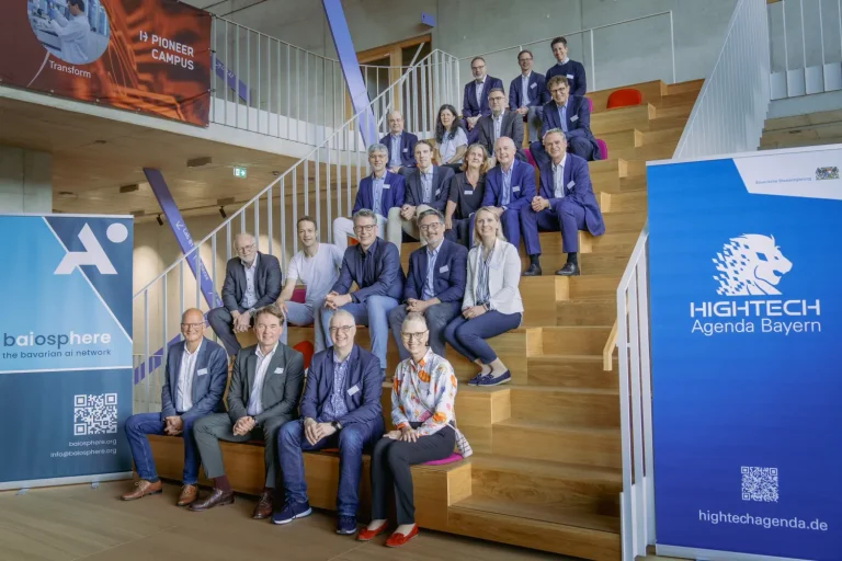 Gruppenbild: auf einer Holztreppe sitzen die Mitglieder des KI-Rats mit Wissenschaftsminister Markus Blume und Dr. Michael Klimke